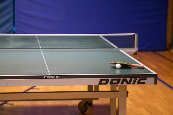 Mesa de tenis de mesa con pala y pelota en un pabellón