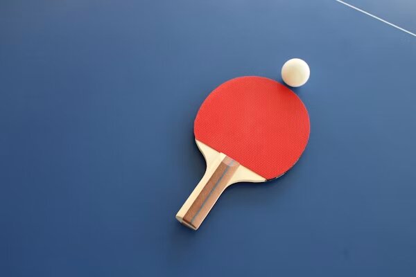 Pala roja y pelota sobre mesa de tenis de mesa azul